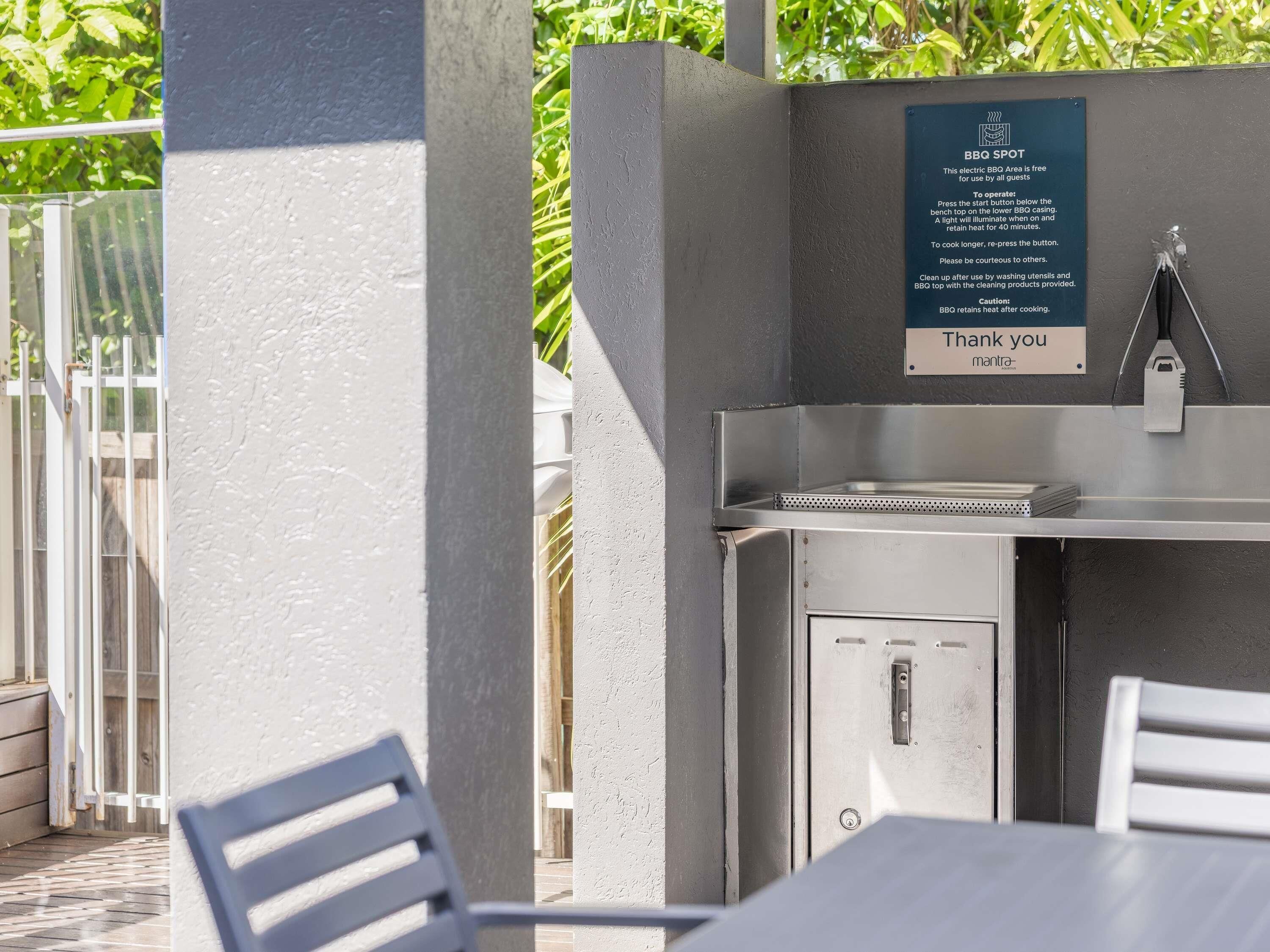 An outdoor BBQ area with a sign, a grill, and a table with chairs.