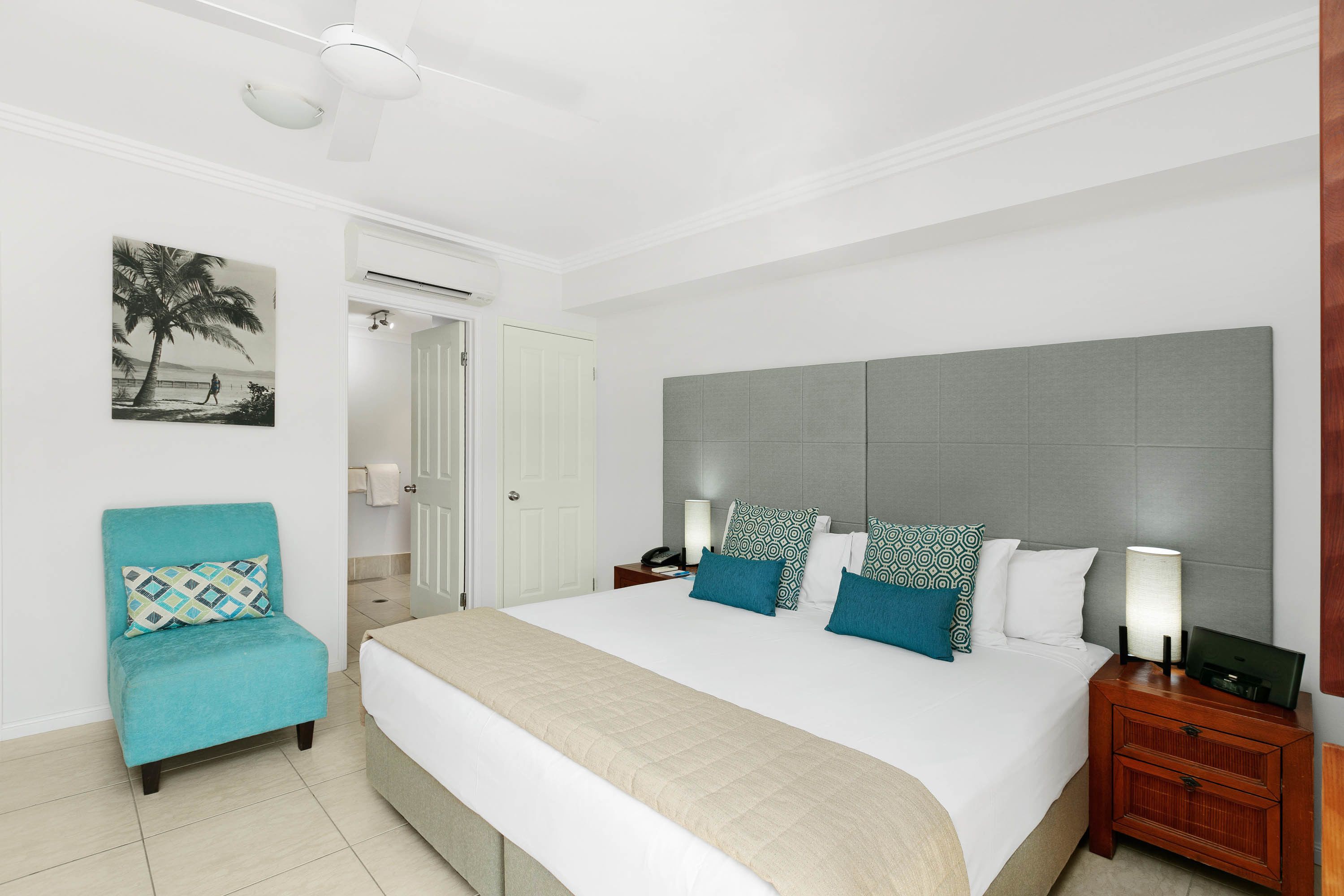 A bedroom with a large bed, a chair, a nightstand, a lamp, and a wall-mounted air conditioning unit.
