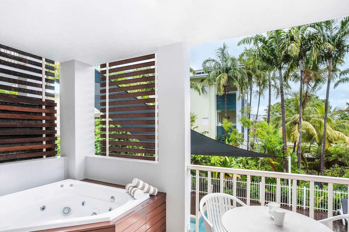 A balcony with a hot tub, white chairs, and a view of palm trees.
