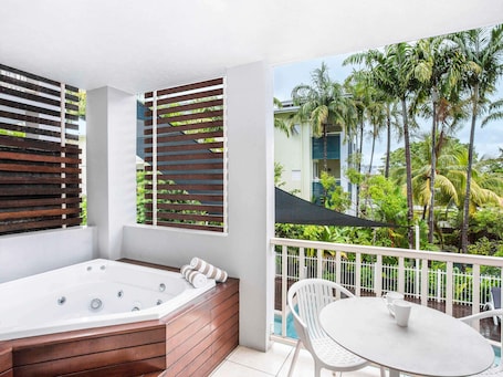 A balcony with a hot tub, white chairs, and a view of palm trees.