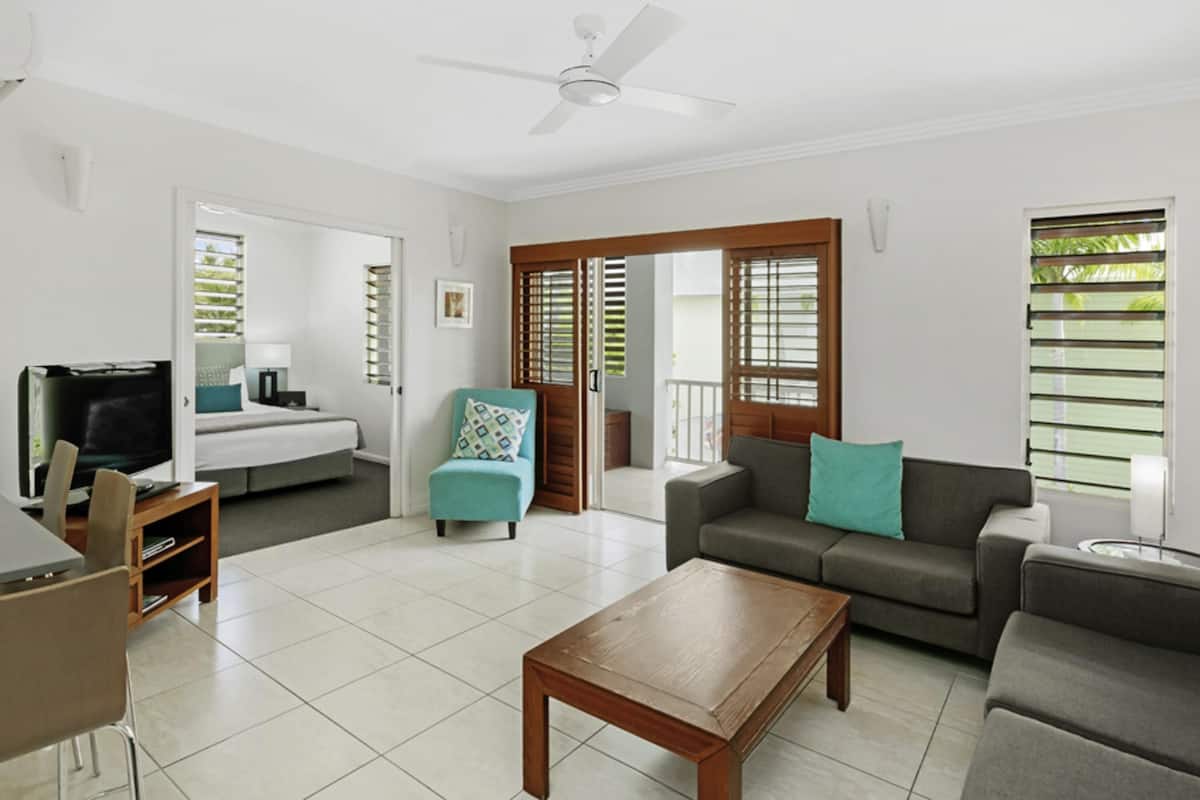 A living room with a television, sofa, coffee table, and a door leading to a balcony.