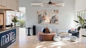 A modern hotel lobby with a reception desk, seating area, ceiling fan, air conditioning units, and artwork on the walls. - Mantra Aqueous on Port (Port Douglas)