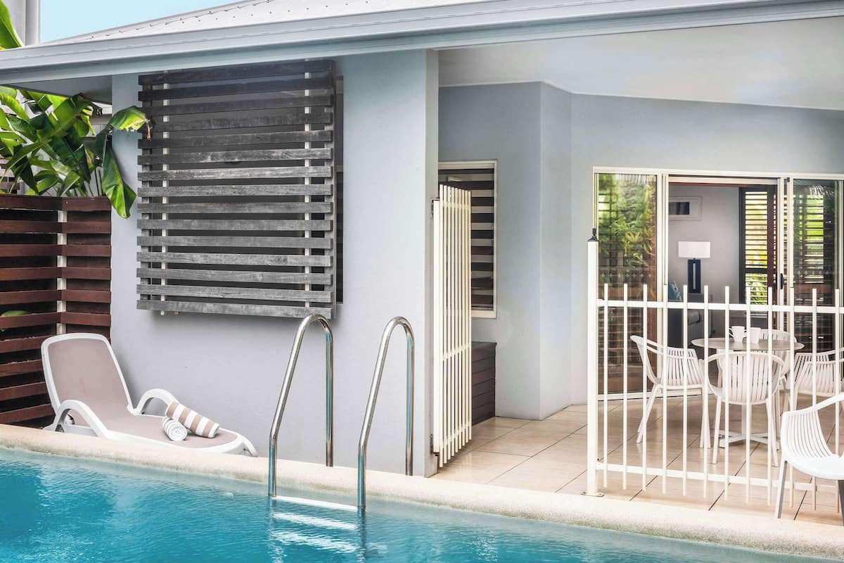 A poolside area with lounge chairs, a pool, and a covered seating area with a table and chairs.