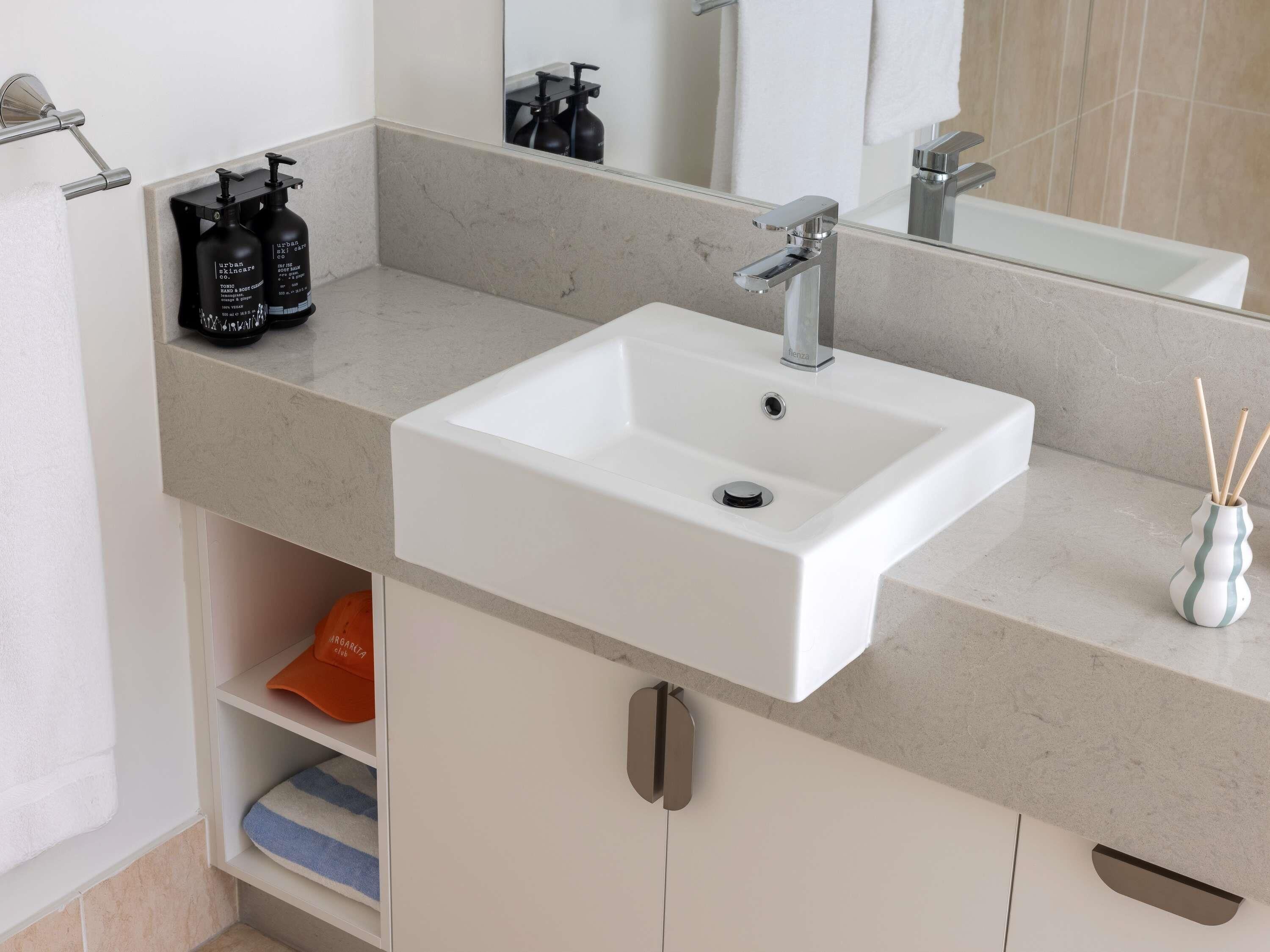 Un bagno con un lavandino bianco, uno specchio e uno scaffale con articoli da toilette.