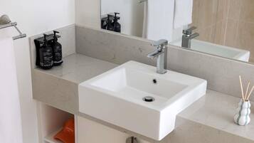 Un baño con un lavabo blanco, un espejo y un estante con artículos de aseo.
