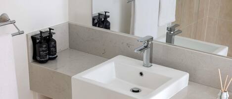 Un bagno con un lavandino bianco, uno specchio e uno scaffale con articoli da toilette.