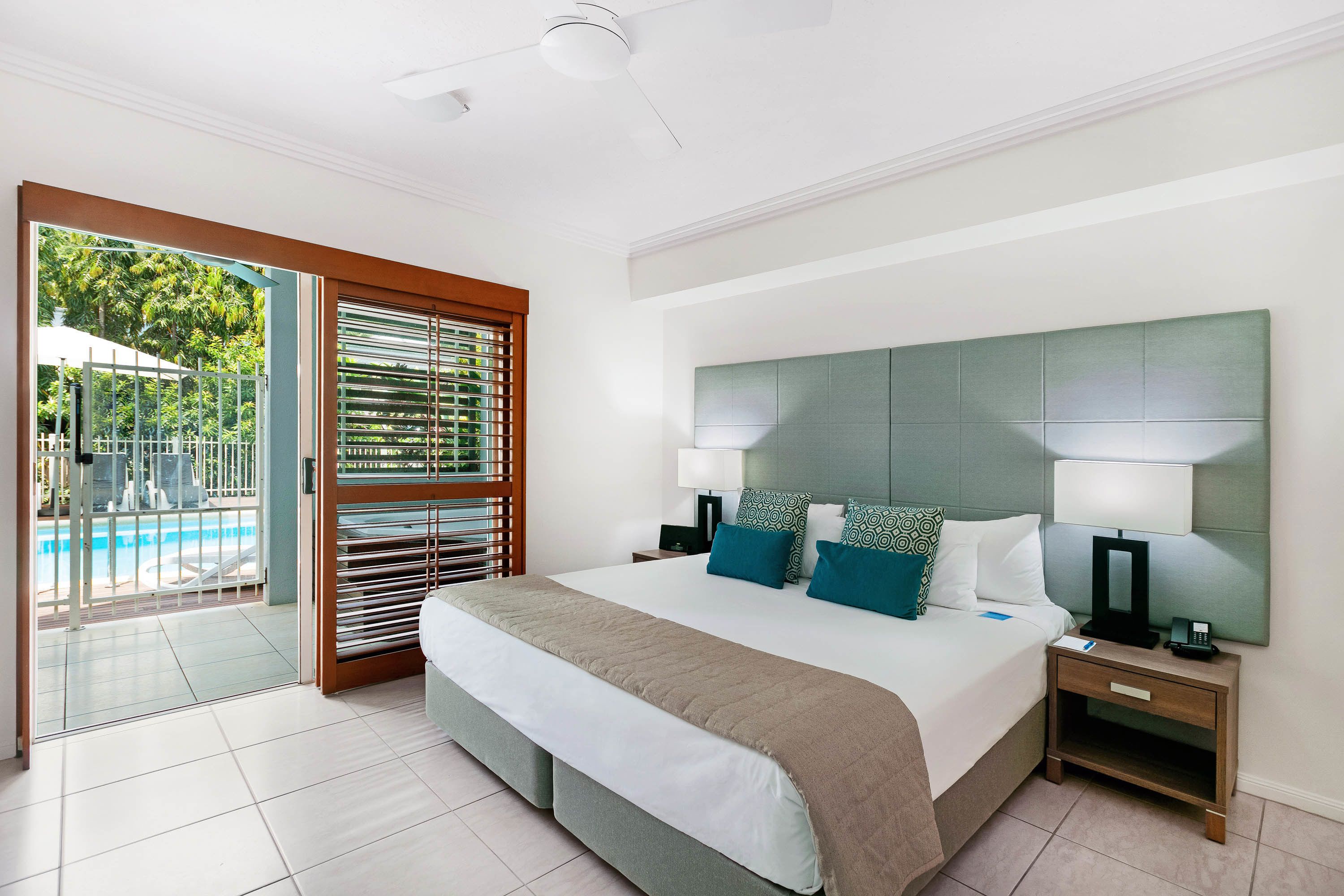 Ein Hotelzimmer mit einem großen Bett, zwei Nachttischen, einem Deckenventilator und Blick auf einen Swimmingpool.