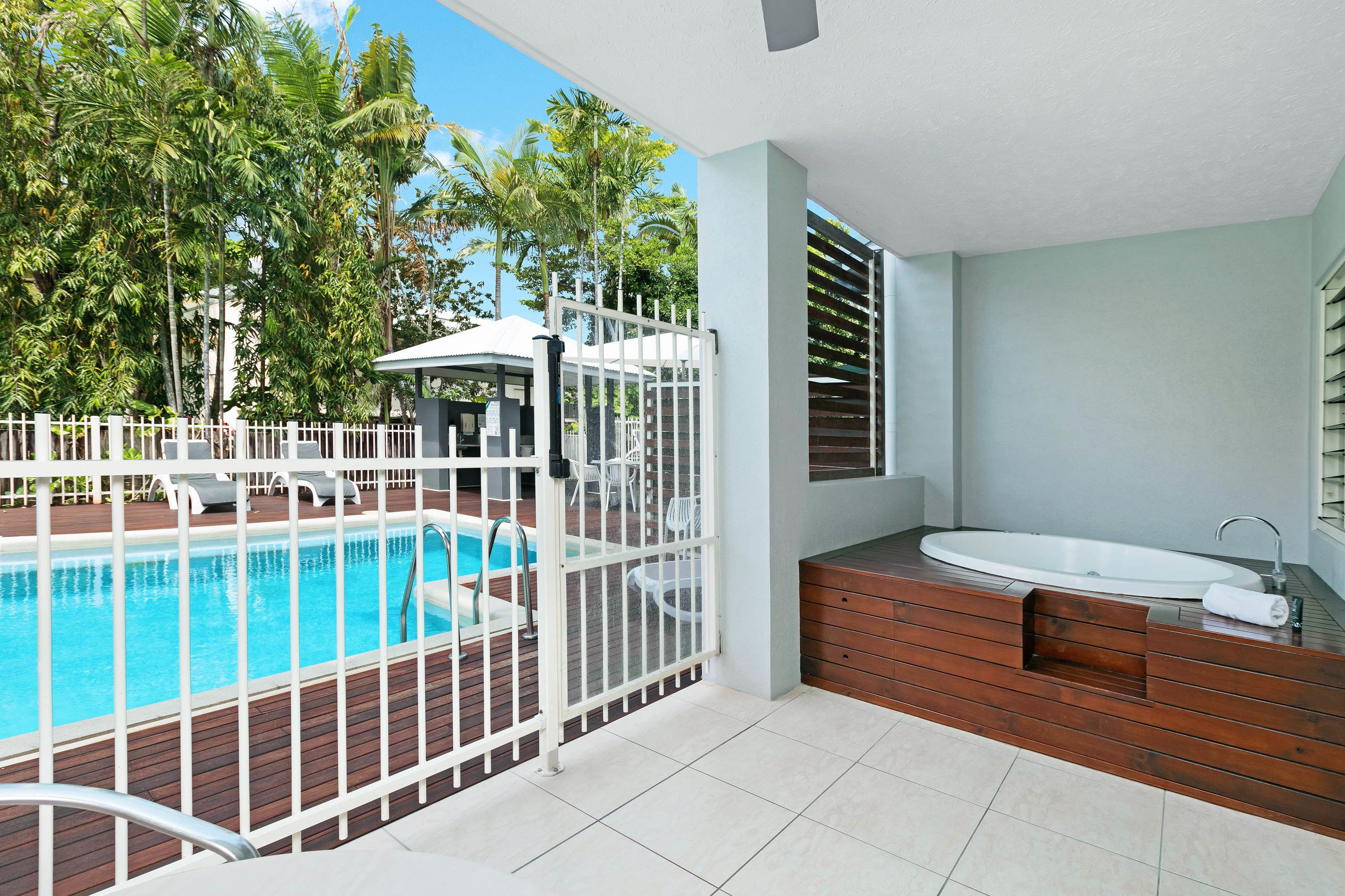 A pool area with a wooden deck, a white fence, and a modern bathroom with a sink and shower.