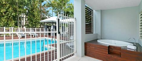 A pool area with a wooden deck, a white fence, and a modern bathroom with a sink and shower.