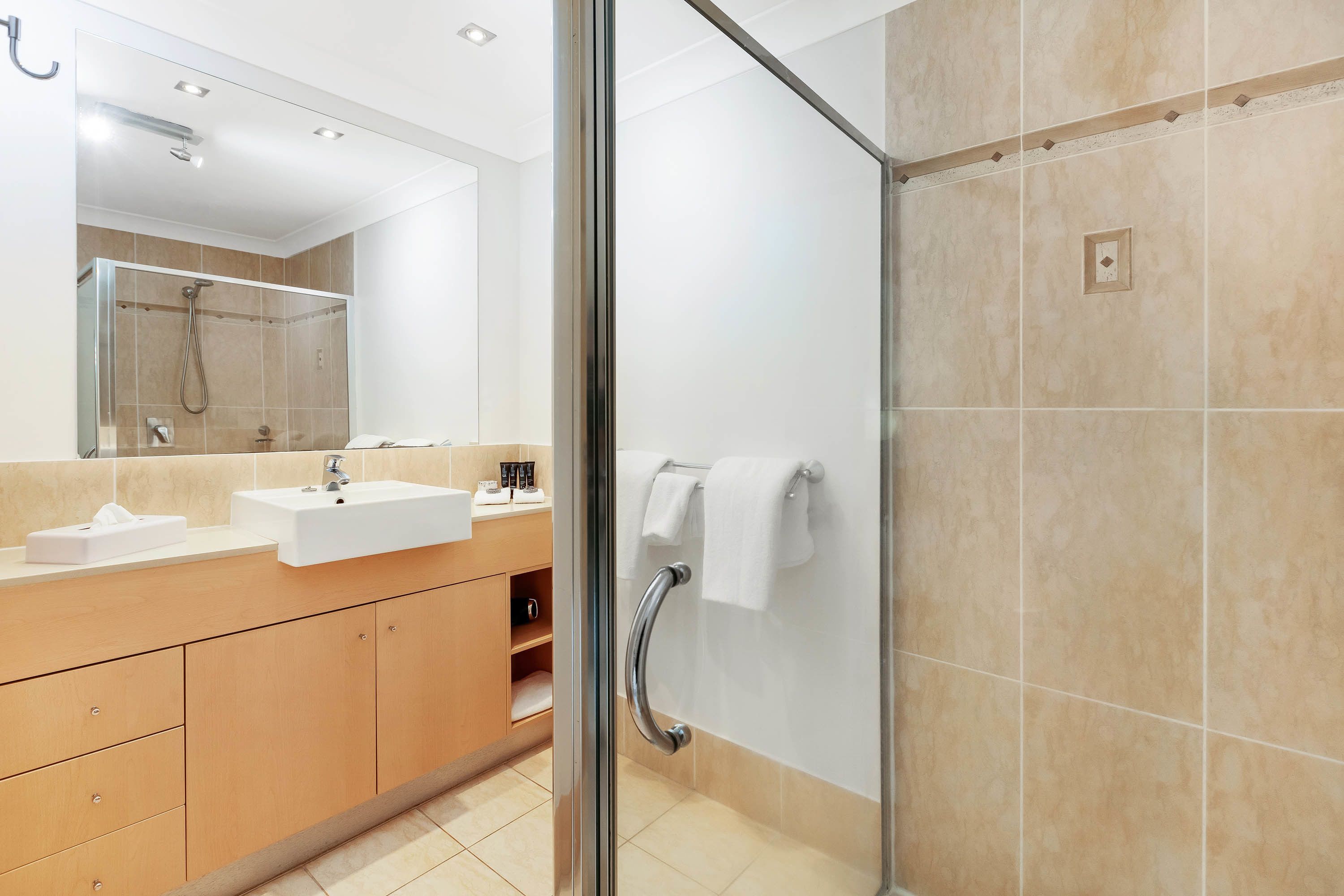 A modern bathroom with a glass shower enclosure, a sink with a mirror, and a towel rack.