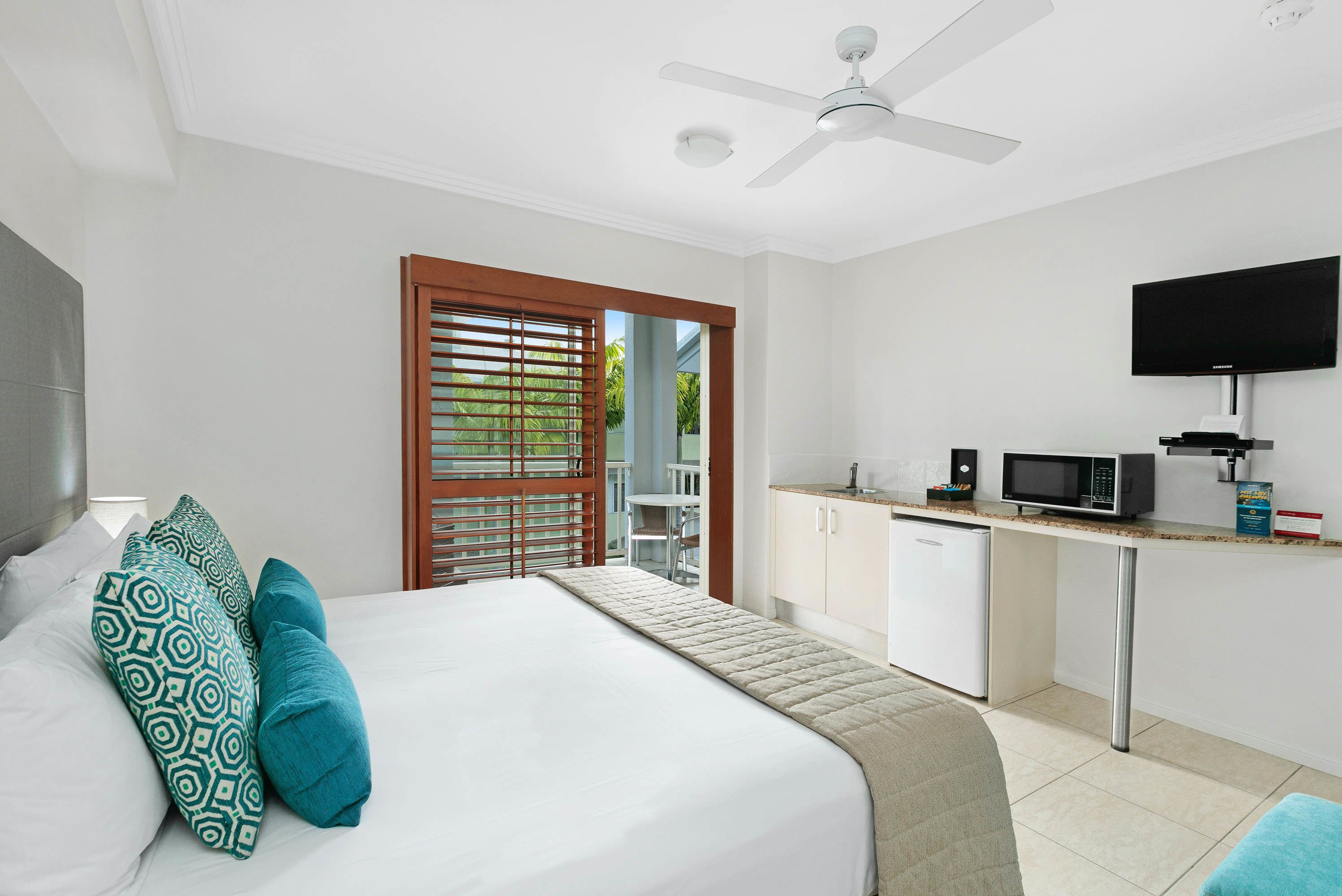 A hotel room with a bed, a desk with a microwave, a TV, and a ceiling fan.
