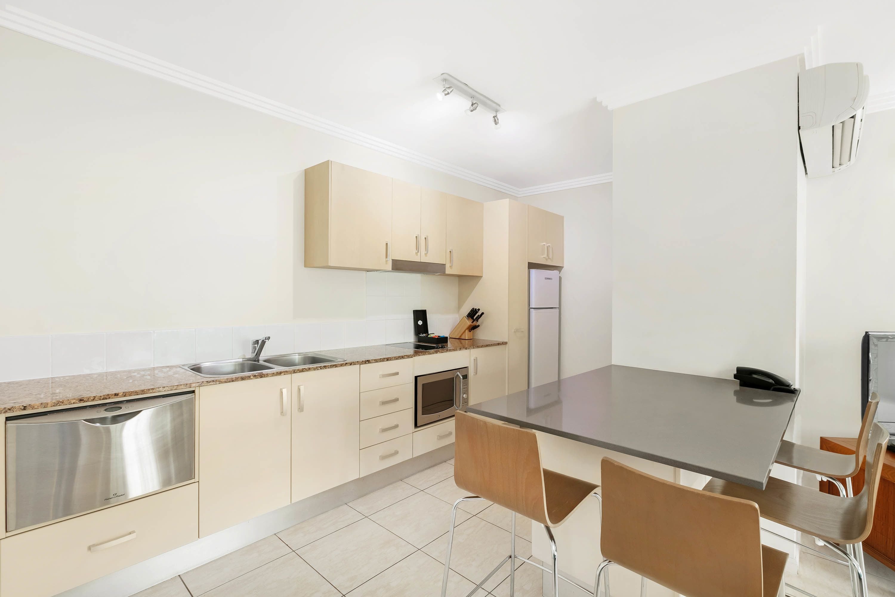 A modern kitchen with a built-in oven, a microwave, and a sink. There is a dining area with a table and chairs.