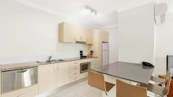A modern kitchen with a built-in oven, a microwave, and a sink. There is a dining area with a table and chairs.