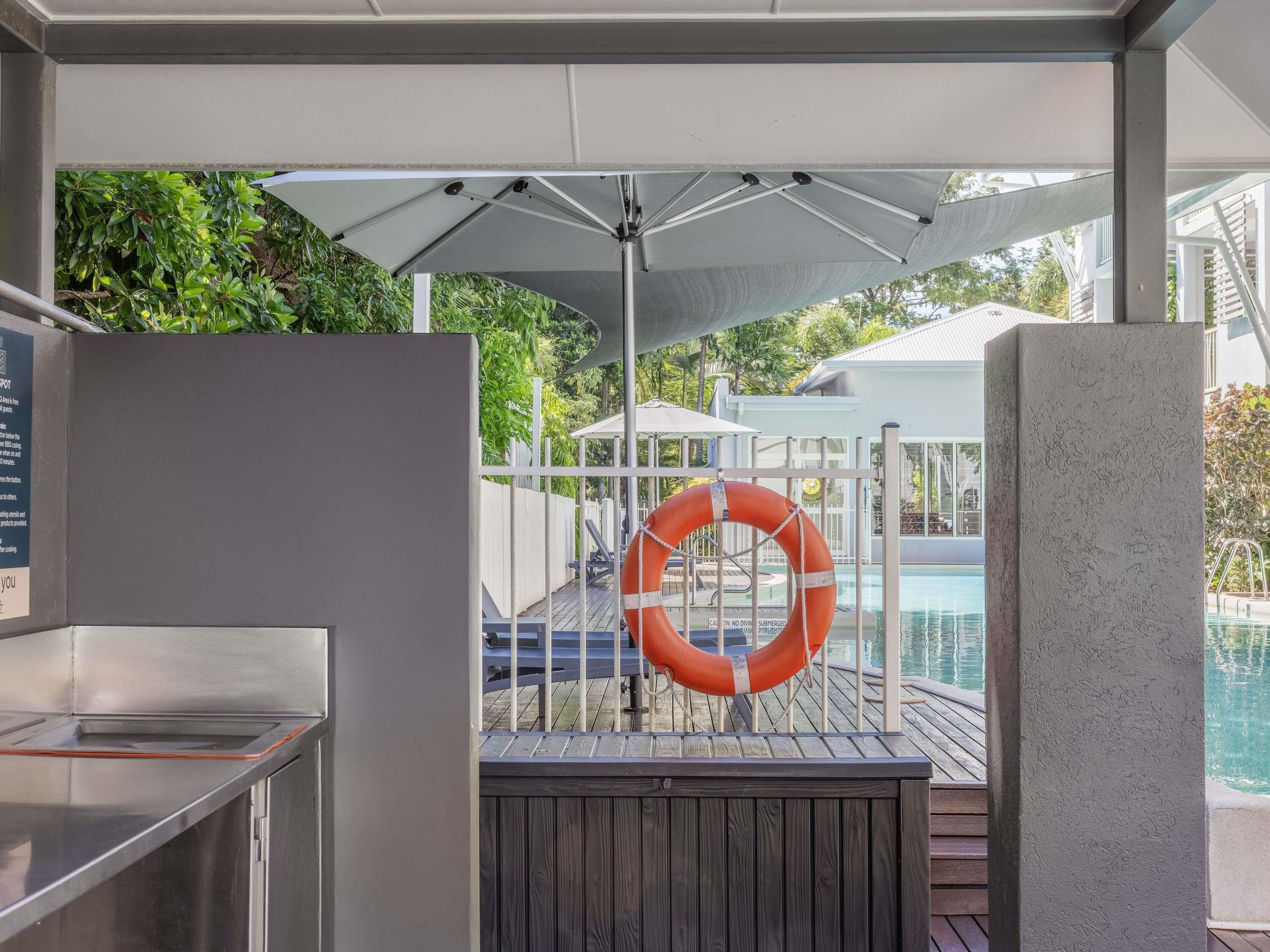 A covered outdoor area with a pool, a lifebuoy, and a grill.