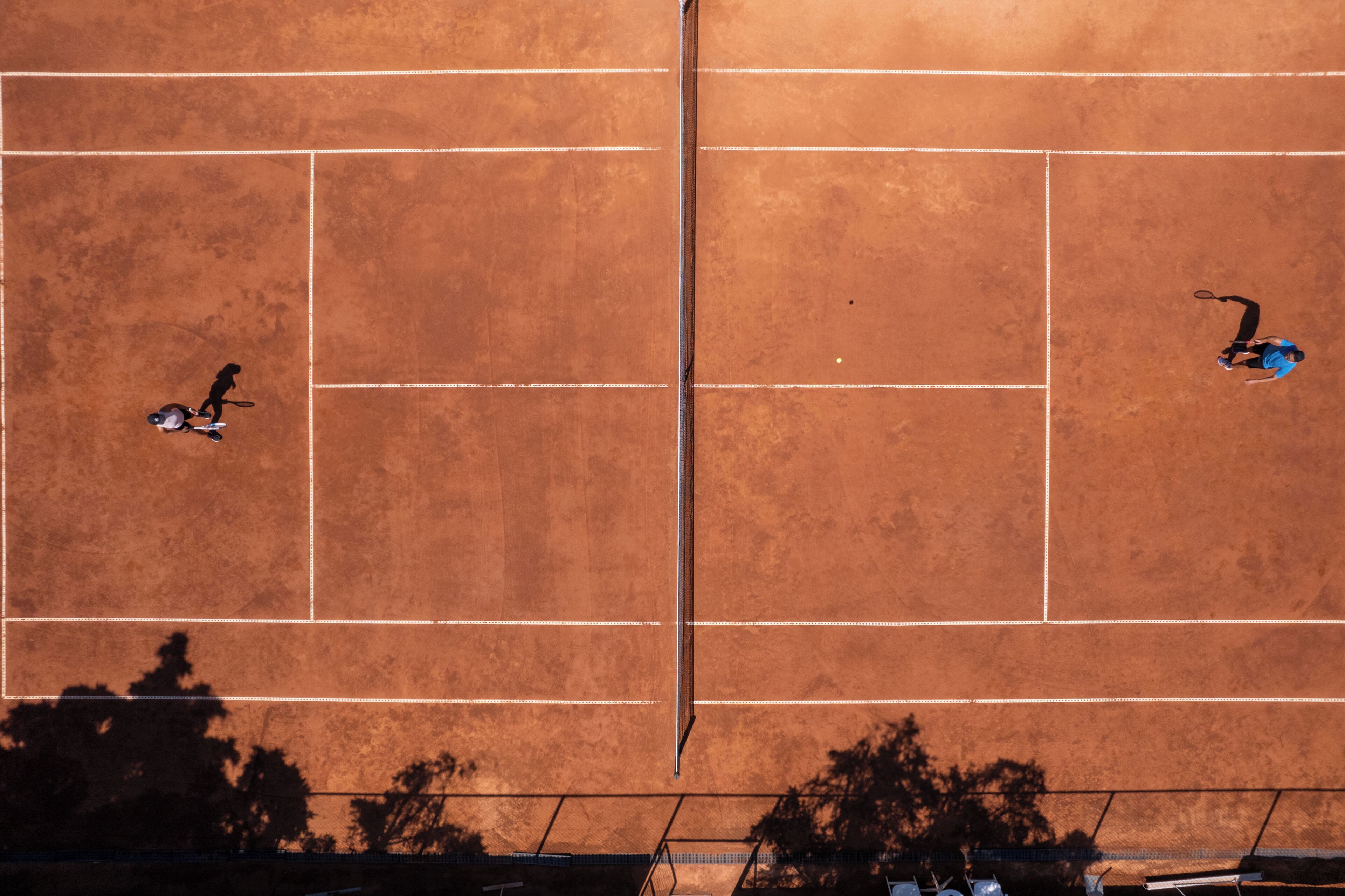 A tennis court with a net in the center, surrounded by a fence.