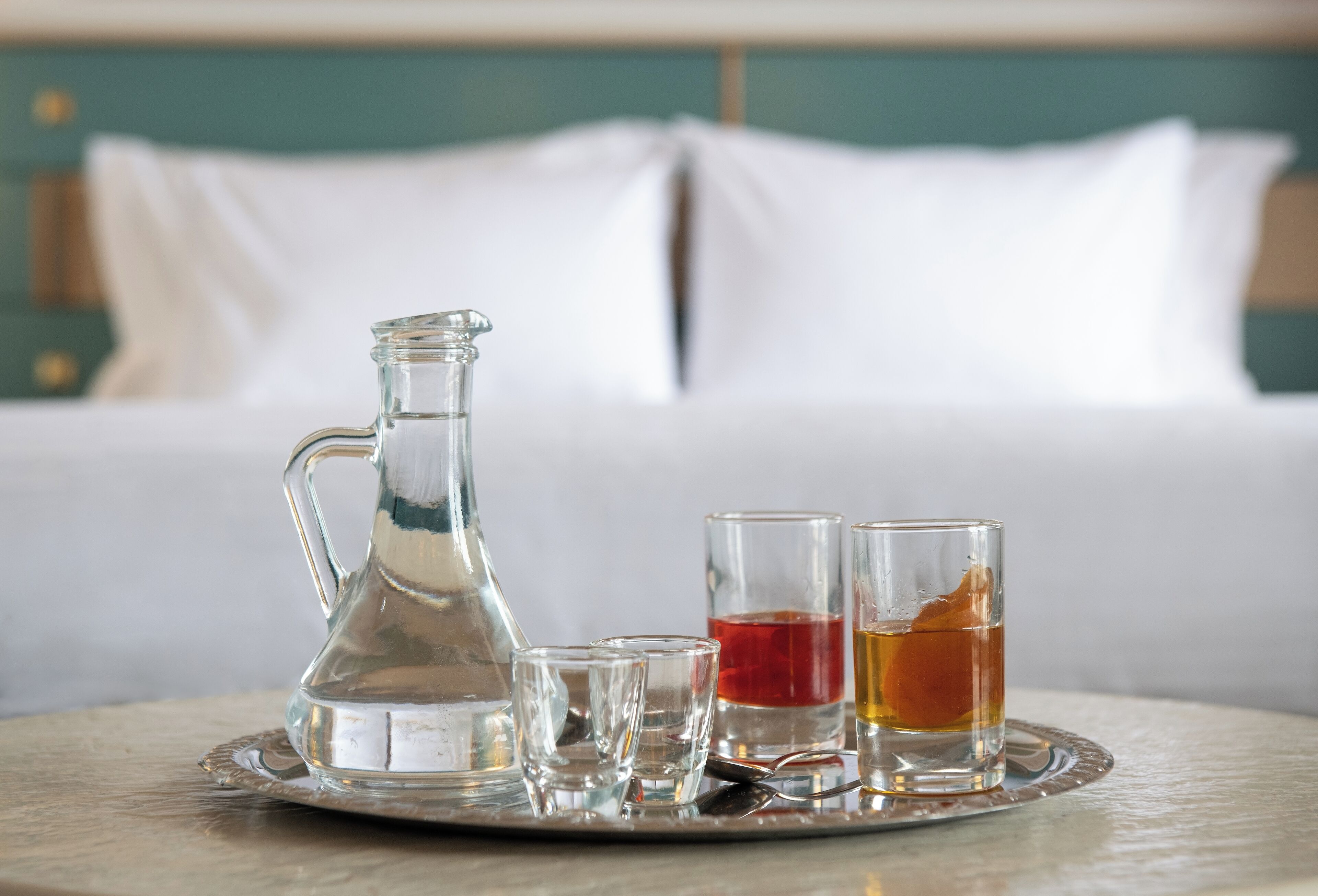 Un plateau avec un pichet en verre, deux verres à shooter et une tasse de thé, posés sur une table dans une chambre d’hôtel.
