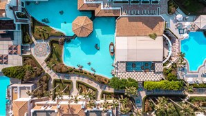 Luchtbeeld van een resort met diverse zwembaden, ligbedden en palmbomen.
