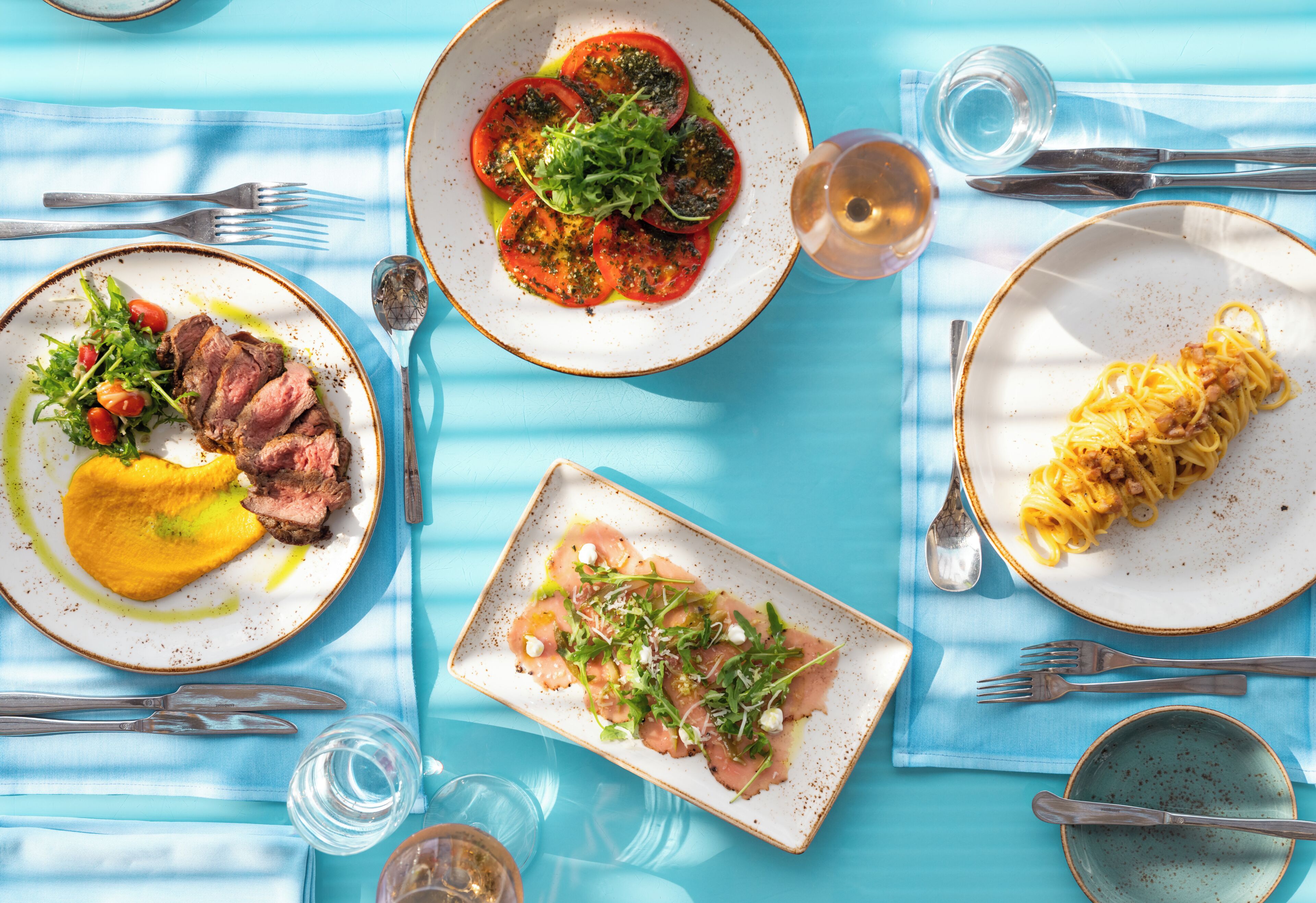 A table set with plates of food, cutlery, and glasses.
