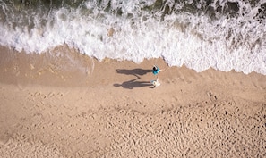 Una playa arenosa con huellas y la sombra de una persona.