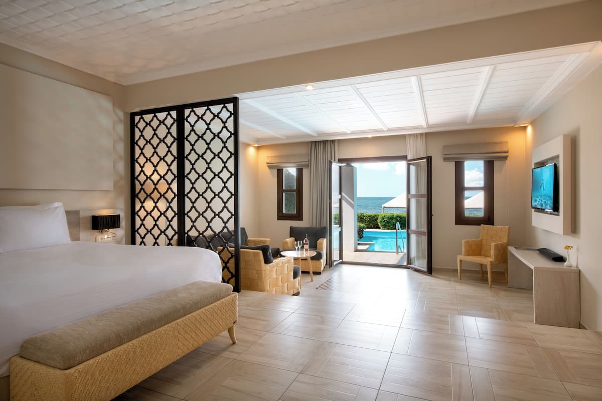 Une chambre d’hôtel spacieuse, dotée d’un grand lit, d’un coin salon avec vue sur la piscine et d’un bureau avec télévision.