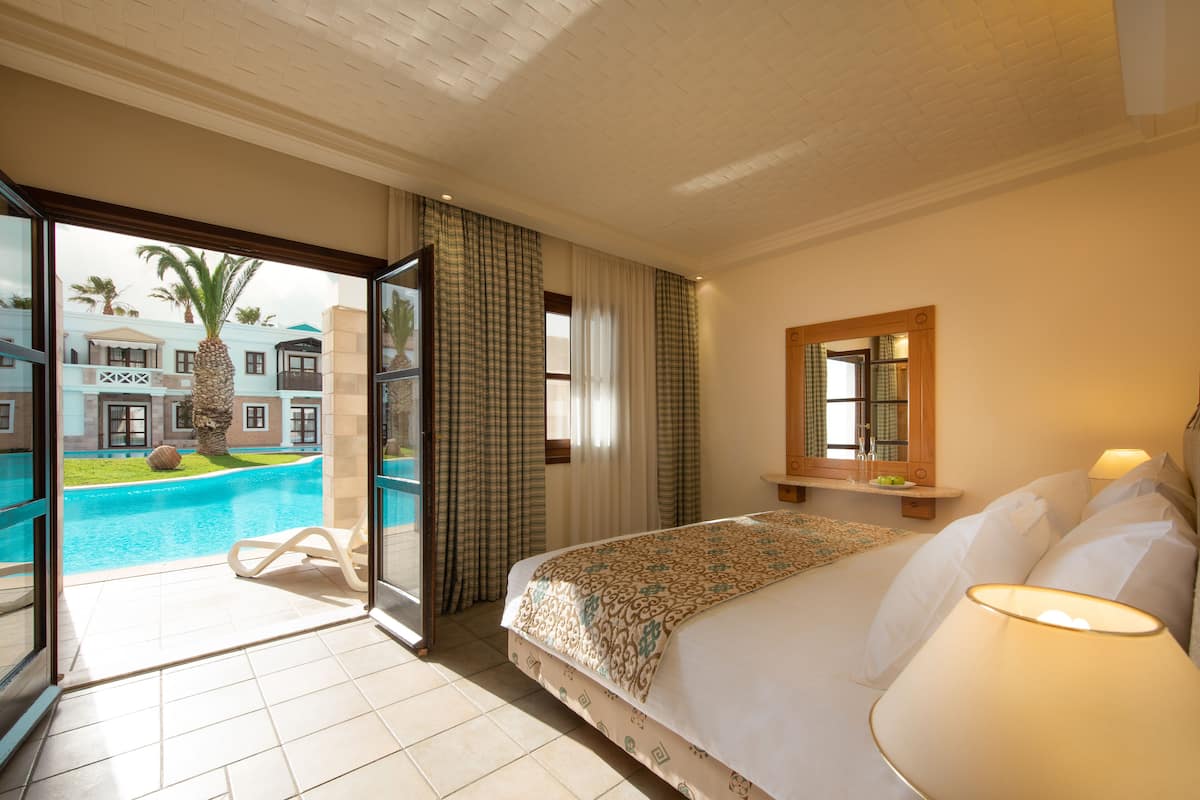 Une chambre d’hôtel avec un lit, une lampe de chevet, une fenêtre avec des rideaux, une vue sur une piscine et un balcon avec une chaise.