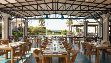 An outdoor dining area with tables and chairs, a covered roof, and a view of the sea.