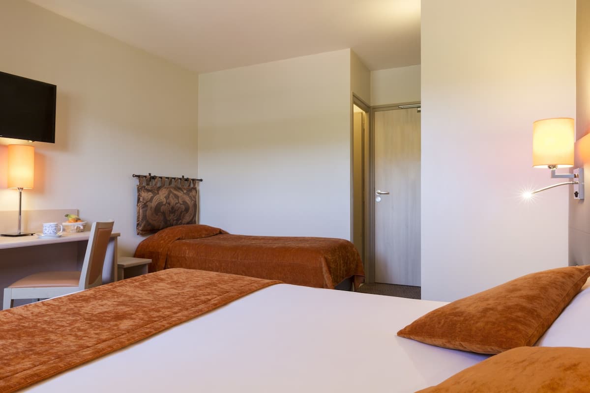 Une chambre d’hôtel avec deux lits, un bureau, une chaise, une télévision et une porte.