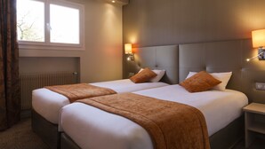 Une chambre d’hôtel avec deux lits, une fenêtre, un radiateur et une table de chevet avec une lampe.