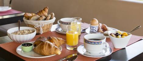 Una mesa de desayuno con cruasanes, cereal, fruta, café y jugo.