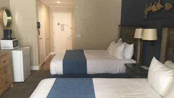A hotel room with two beds, a microwave, a coffee maker, and a door leading to another room.