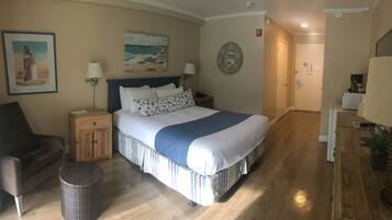 A hotel room with a bed, nightstands, a chair, a waste basket, and a painting on the wall.