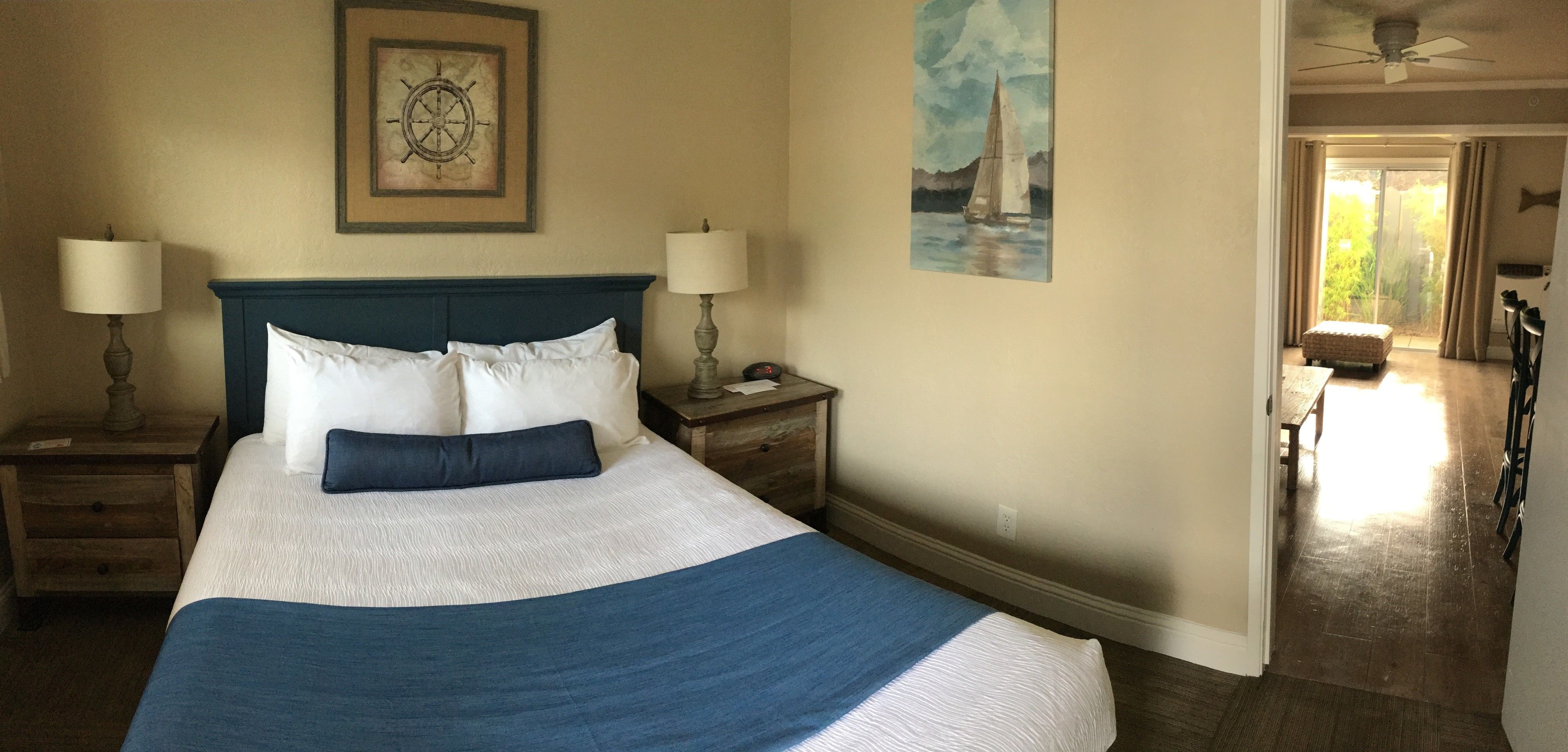 Un lit bien fait, recouvert d’une couvre-lit bleue et blanche, avec deux lampes de chevet et un tableau représentant un voilier accroché au mur.