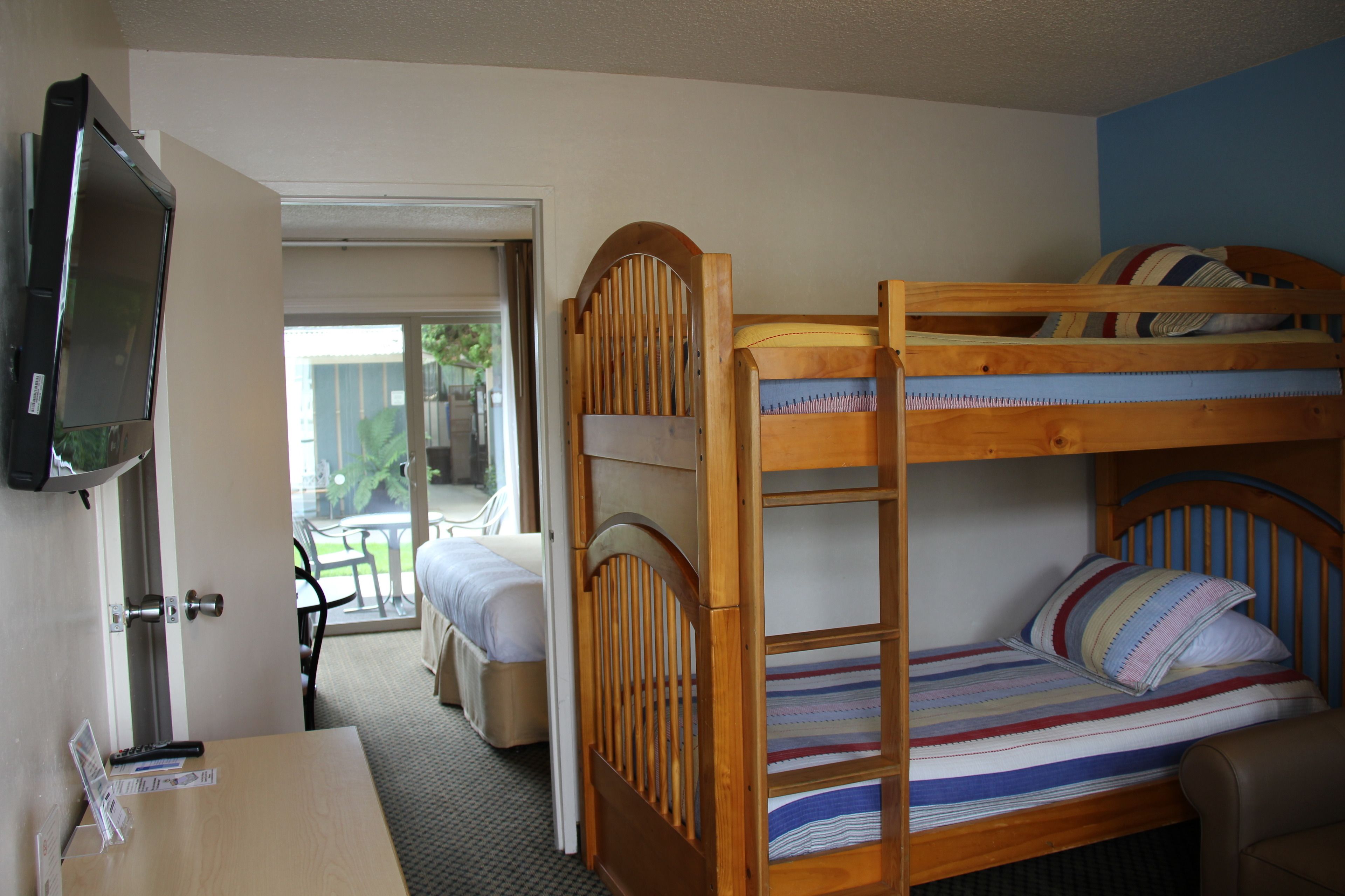 A bunk bed with a TV mounted on the wall, a desk, and a view of the outside.