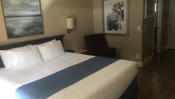 A hotel room with a large bed, a nightstand, a chair, and artwork on the walls.