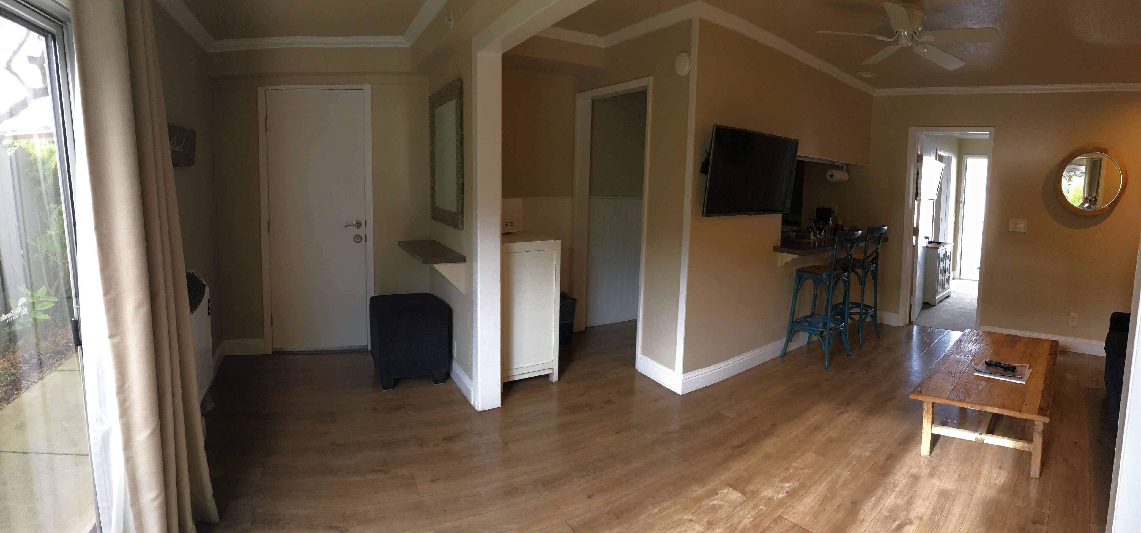 A spacious living room with hardwood flooring, a ceiling fan, a TV mounted on the wall, and a wooden coffee table.