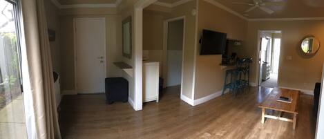 A spacious living room with hardwood flooring, a ceiling fan, a TV mounted on the wall, and a wooden coffee table.