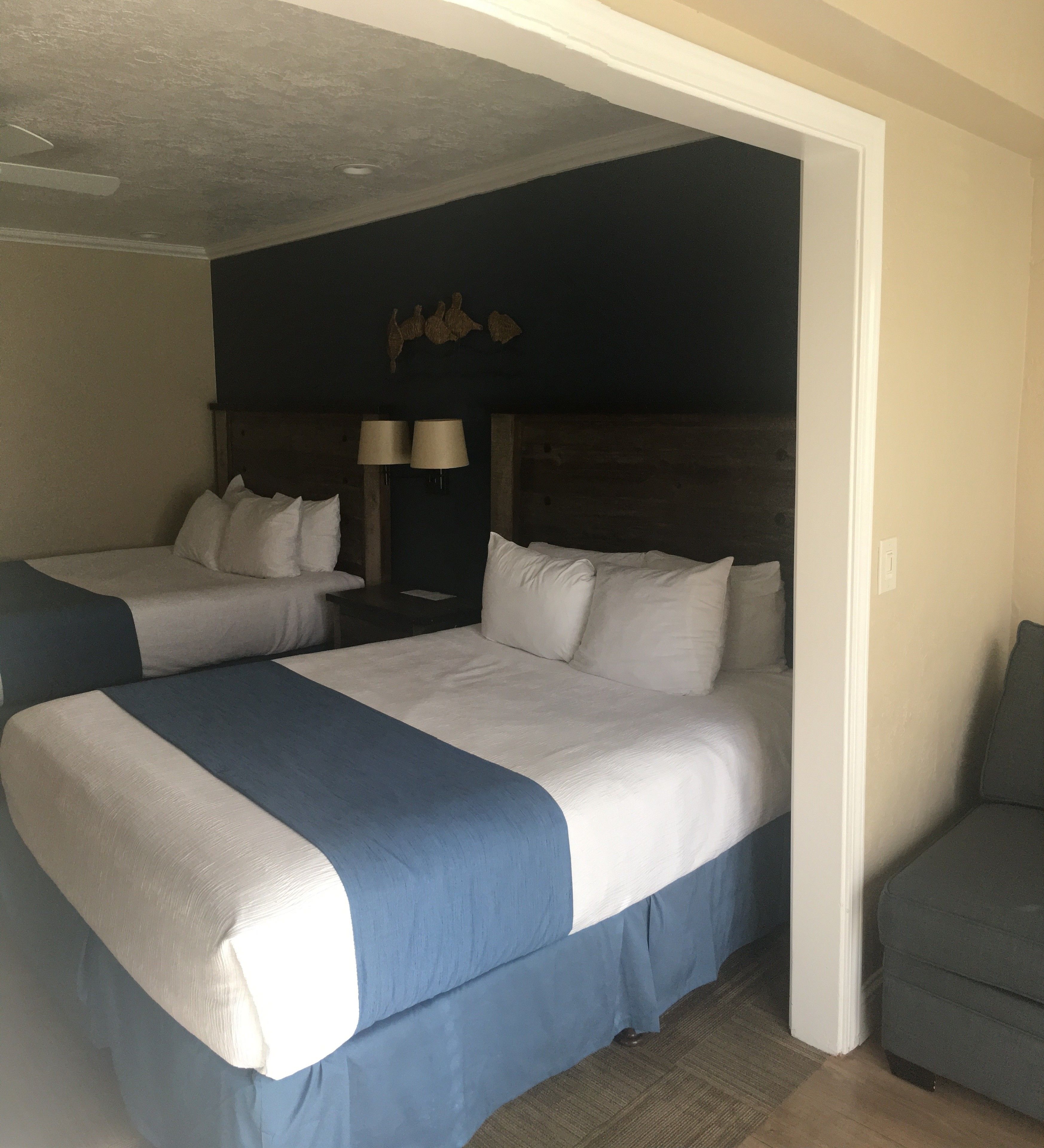 Une chambre d’hôtel avec deux lits, une tête de lit sombre et un petit coin salon.