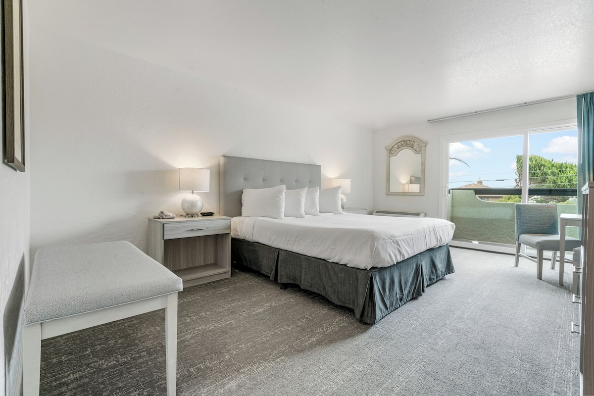 Een hotelkamer met een bed, nachtkastjes, een stoel en een balkon met uitzicht.