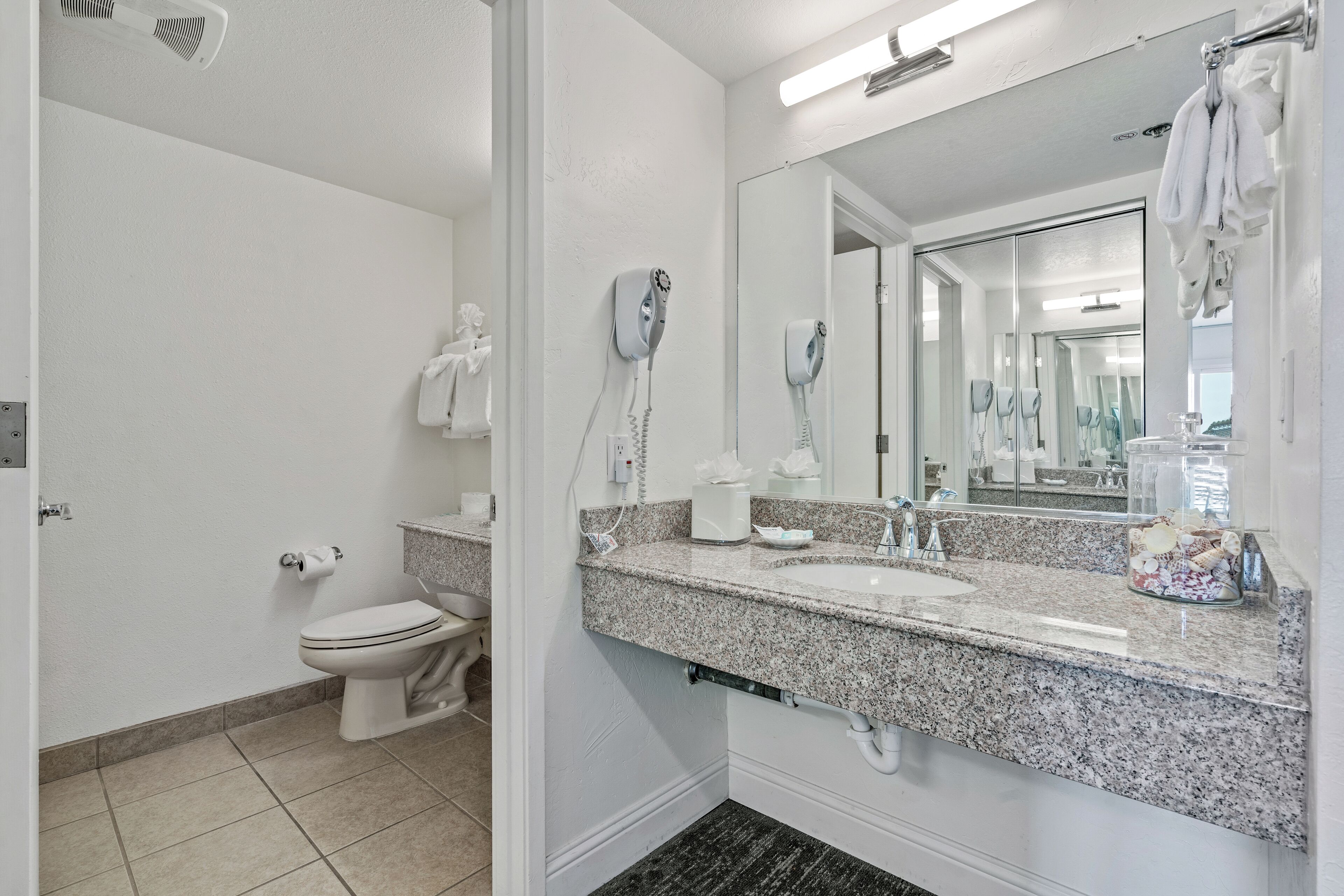 A bathroom with a toilet, two hair dryers, a sink, and a large mirror.