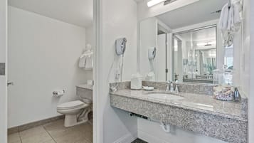 A bathroom with a toilet, two hair dryers, a sink, and a large mirror.