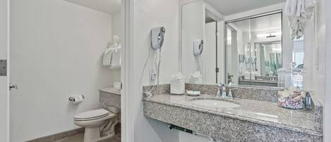 A bathroom with a toilet, two hair dryers, a sink, and a large mirror.