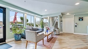 A spacious living area with a sofa, armchairs, and a coffee table. There is a large window with a view of the outside, a potted plant, and a staircase leading to another level. - La Serena Inn (Morro Bay)