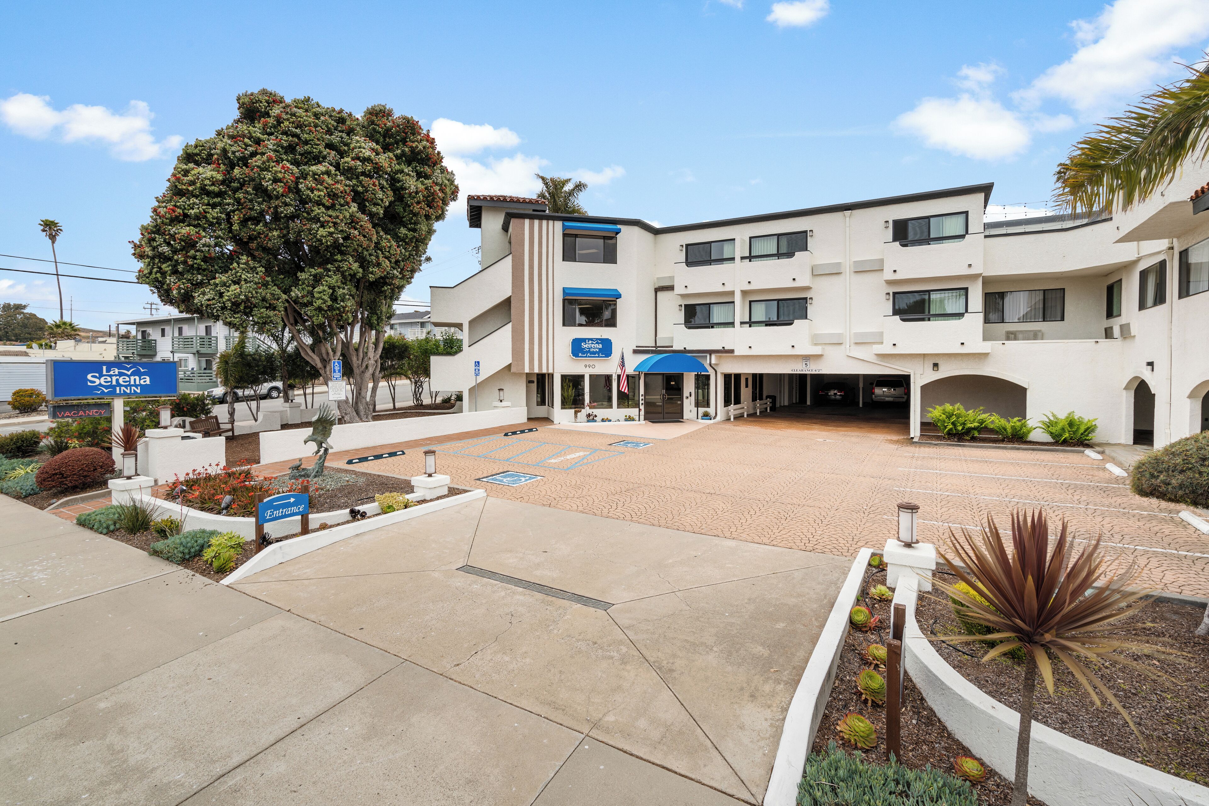 A hotel with a central courtyard, a large tree, and a sign for La Serena Inn.