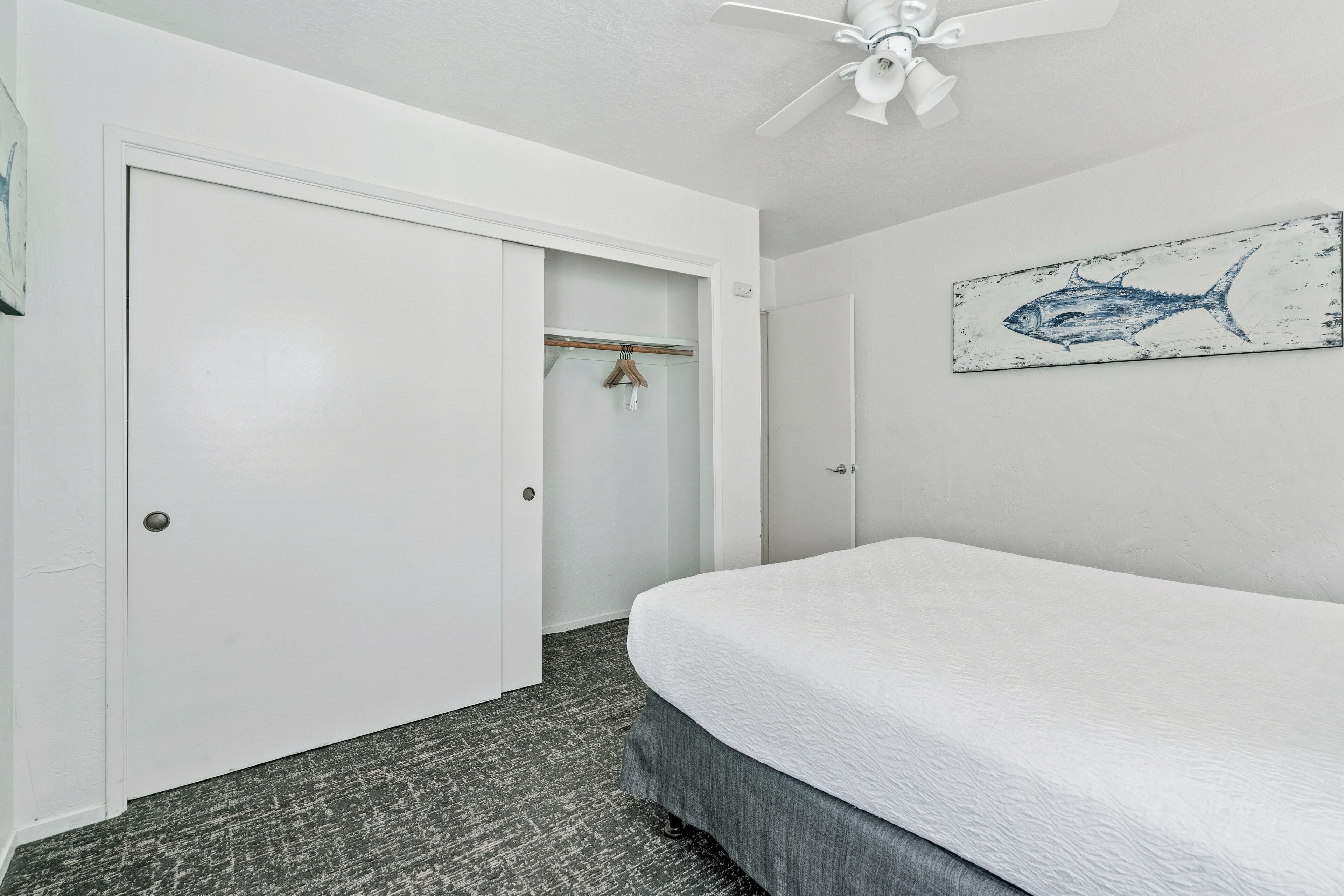 A bedroom with a bed, a white door, a closet, and a ceiling fan.