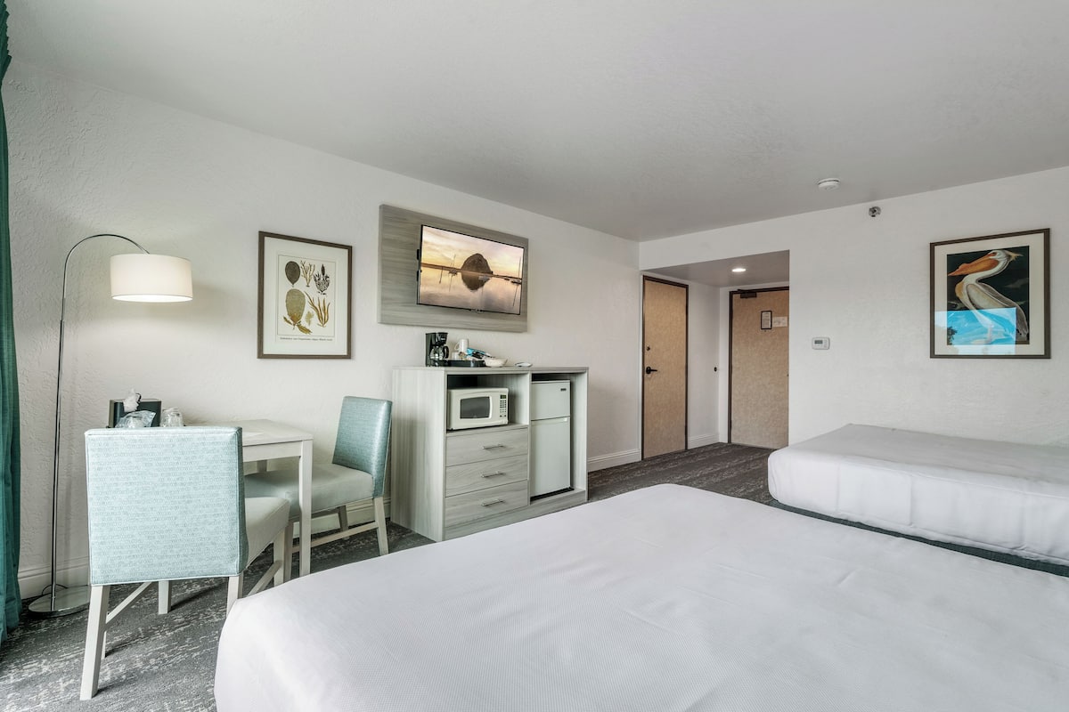 Een hotelkamer met een bed, een bureau met een stoel, een magnetron en een televisie.