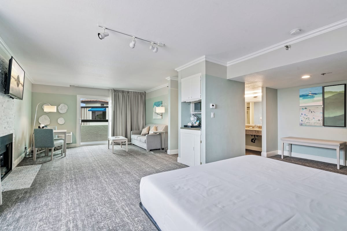 Een hotelkamer met een groot bed, een bureau met stoel, een bank, een kleine tafel en een open haard. In de achtergrond is een badkamer zichtbaar.