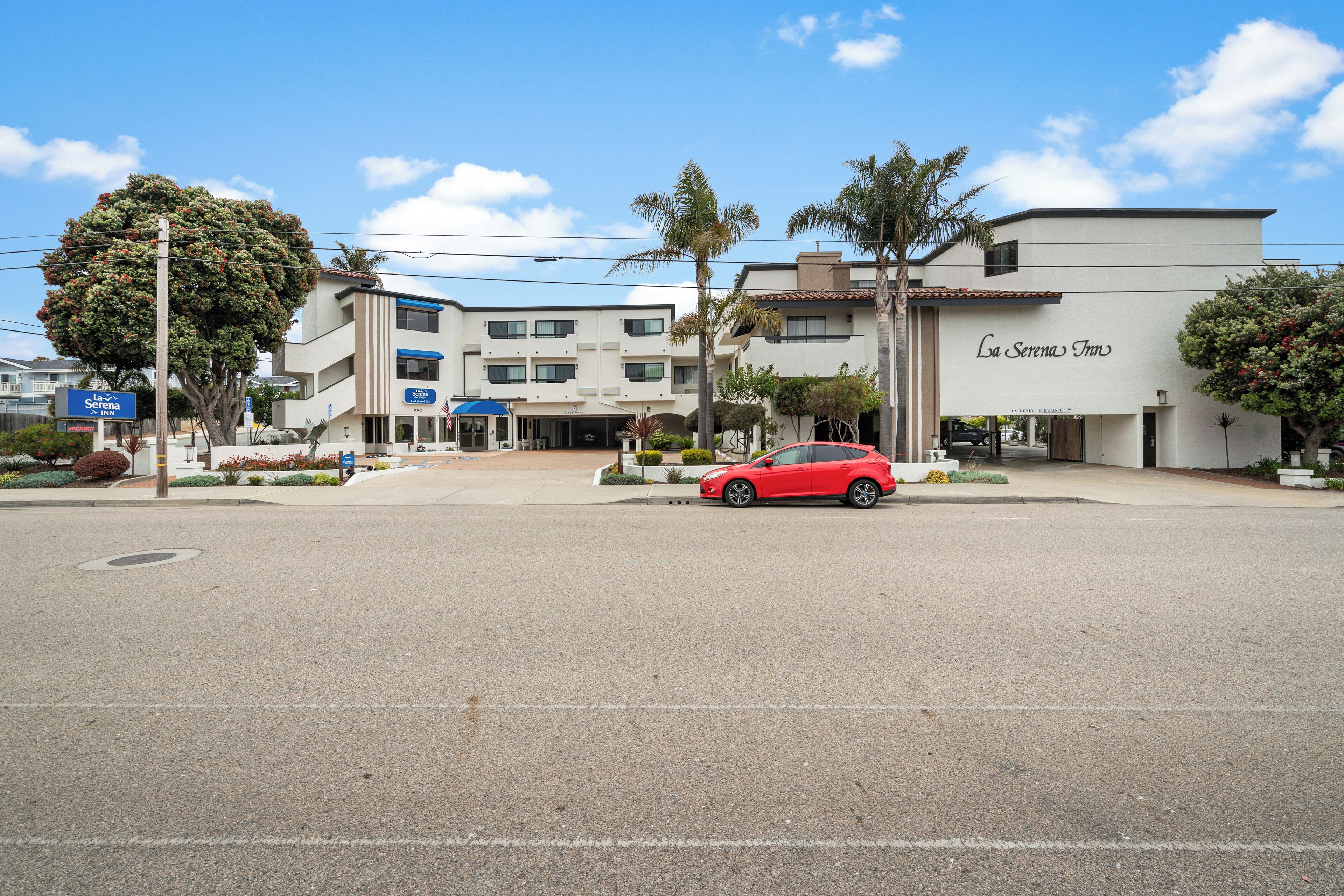 Un hôtel à la façade moderne, une voiture rouge garée devant, et un ciel bleu azur.
