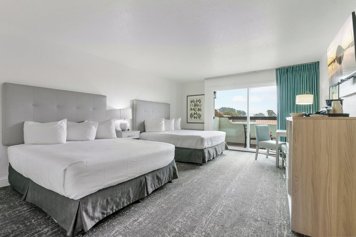 Een hotelkamer met twee bedden, een bureau, een stoel en uitzicht op de omgeving.