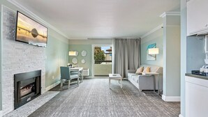 A modern living room with a fireplace, a flat-screen TV mounted on a brick wall, a dining area with a table and chairs, and a sofa. - La Serena Inn (Morro Bay)