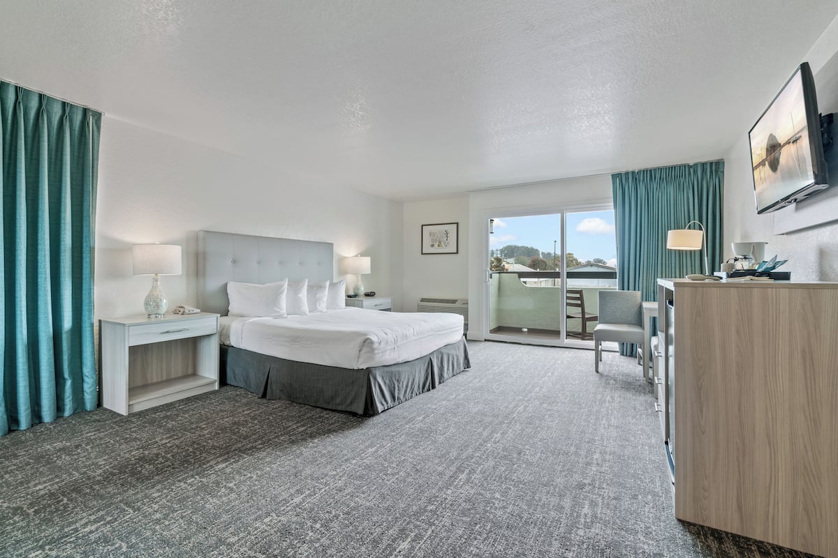 Een hotelkamer met een bed, nachtkastjes, een bureau, een stoel en een groot raam.